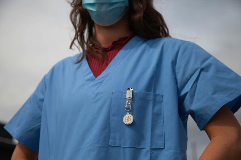 A nurse standing at the ready, wearing scrubs with a MedicAlert ID attached.